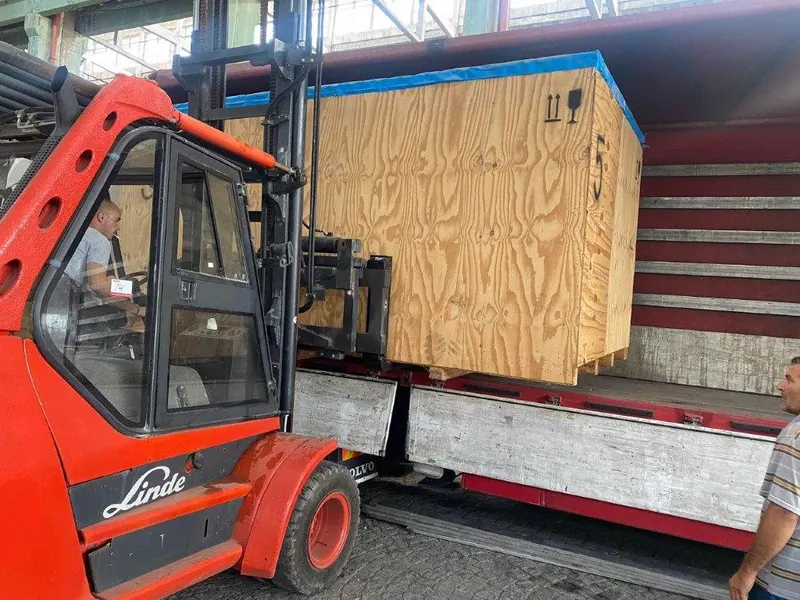 Forklift with long forks unloading a large crate